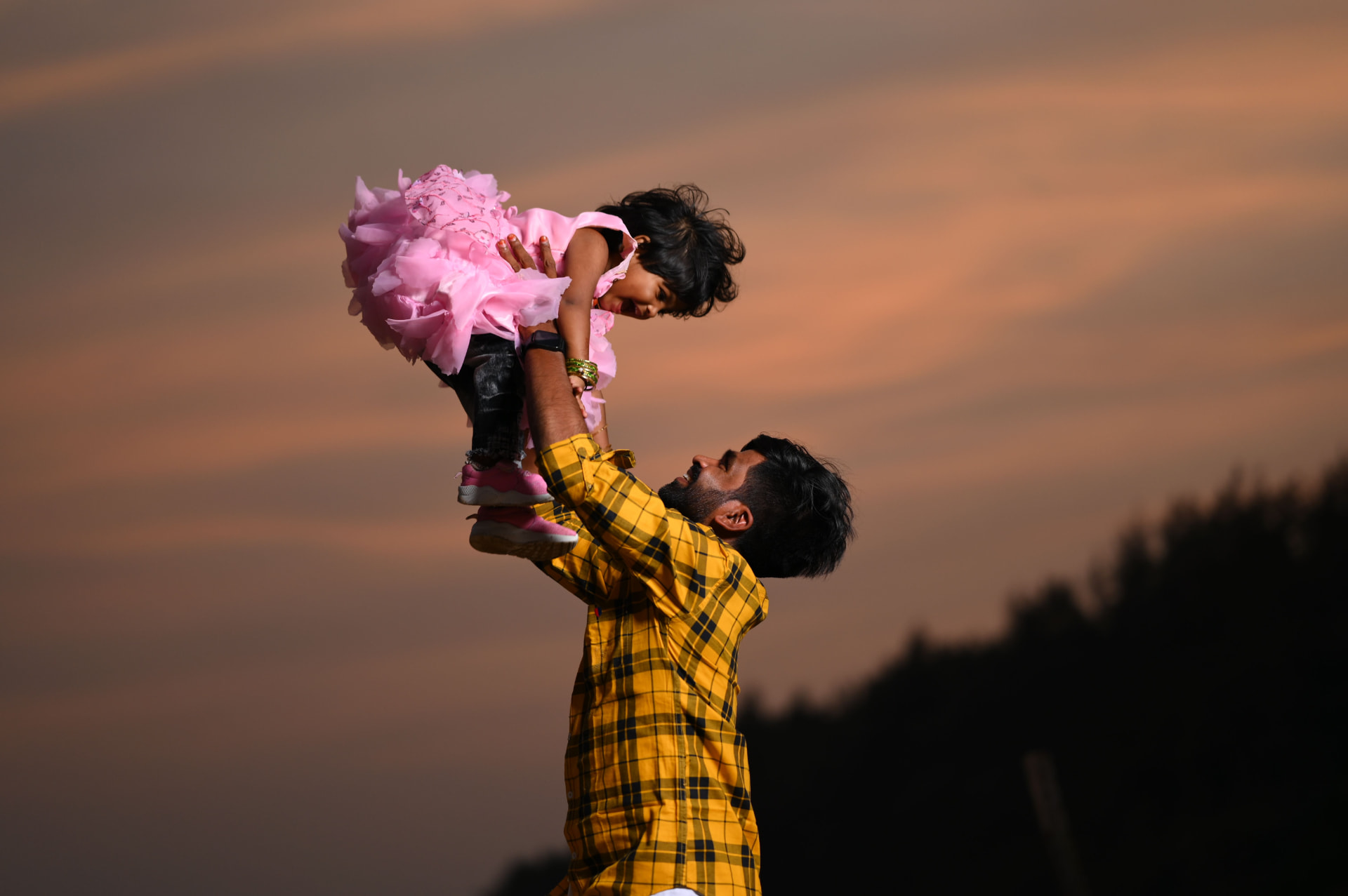 A father lifting his daughter into the air at sunset